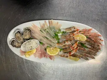 Piatto di cruditè con ostriche, gamberi, carpaccio di pesce e fettine di limone serviti su vassoio ovale