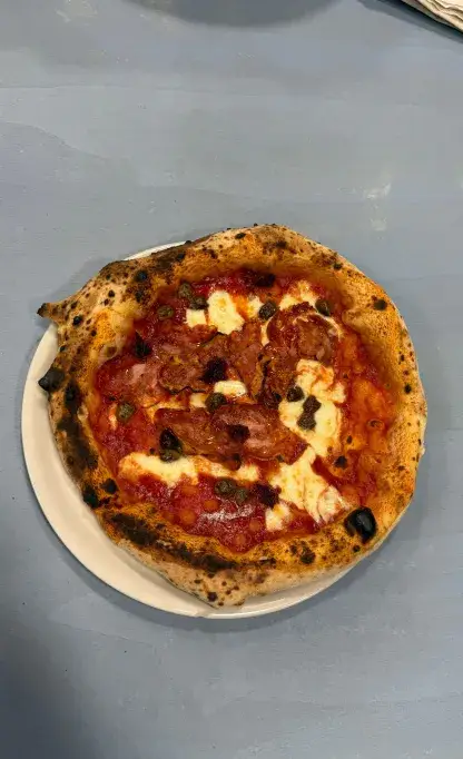 Pizza napoletana con salame piccante, capperi e mozzarella fusa su base di pomodoro