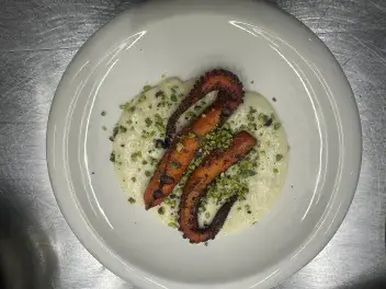 Tentacoli di polpo grigliato serviti su crema di patate vellutata e guarniti con granella di pistacchi